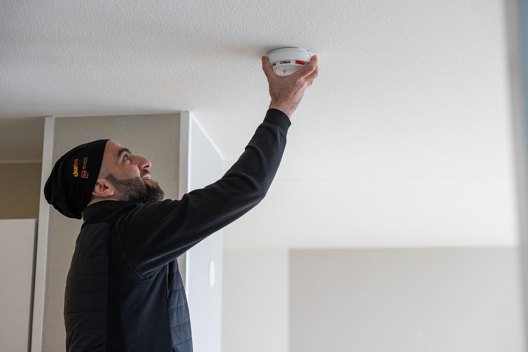 En kille i svart håller upp en brandvarnare mot taket