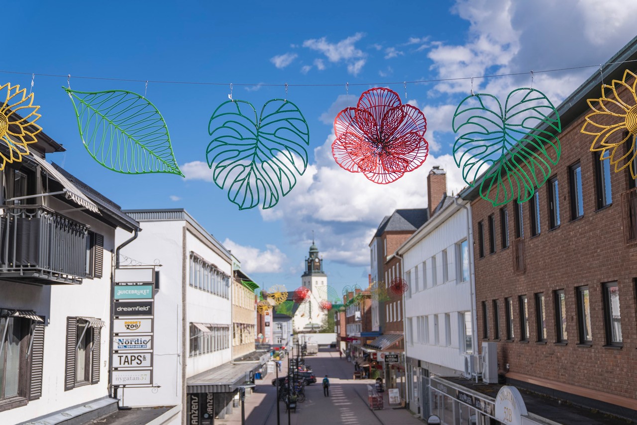 Stadsgata med byggnader och färgglada bladdekorationer ovanför.